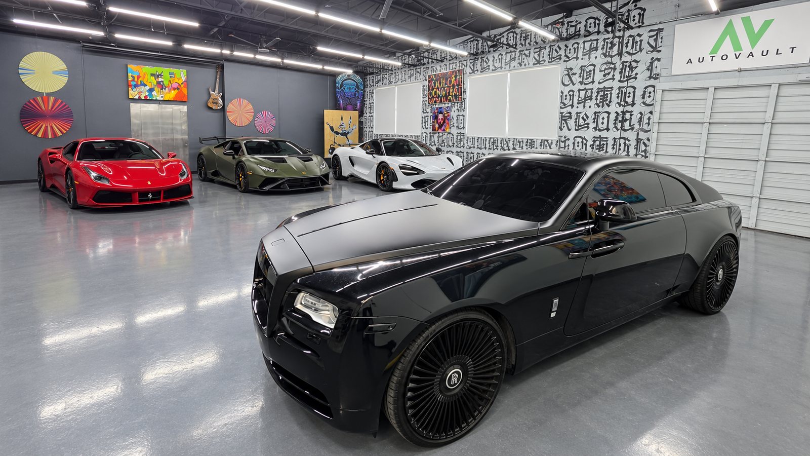 A black Rolls-Royce Wraith on the polished floor under the AutoVault sign