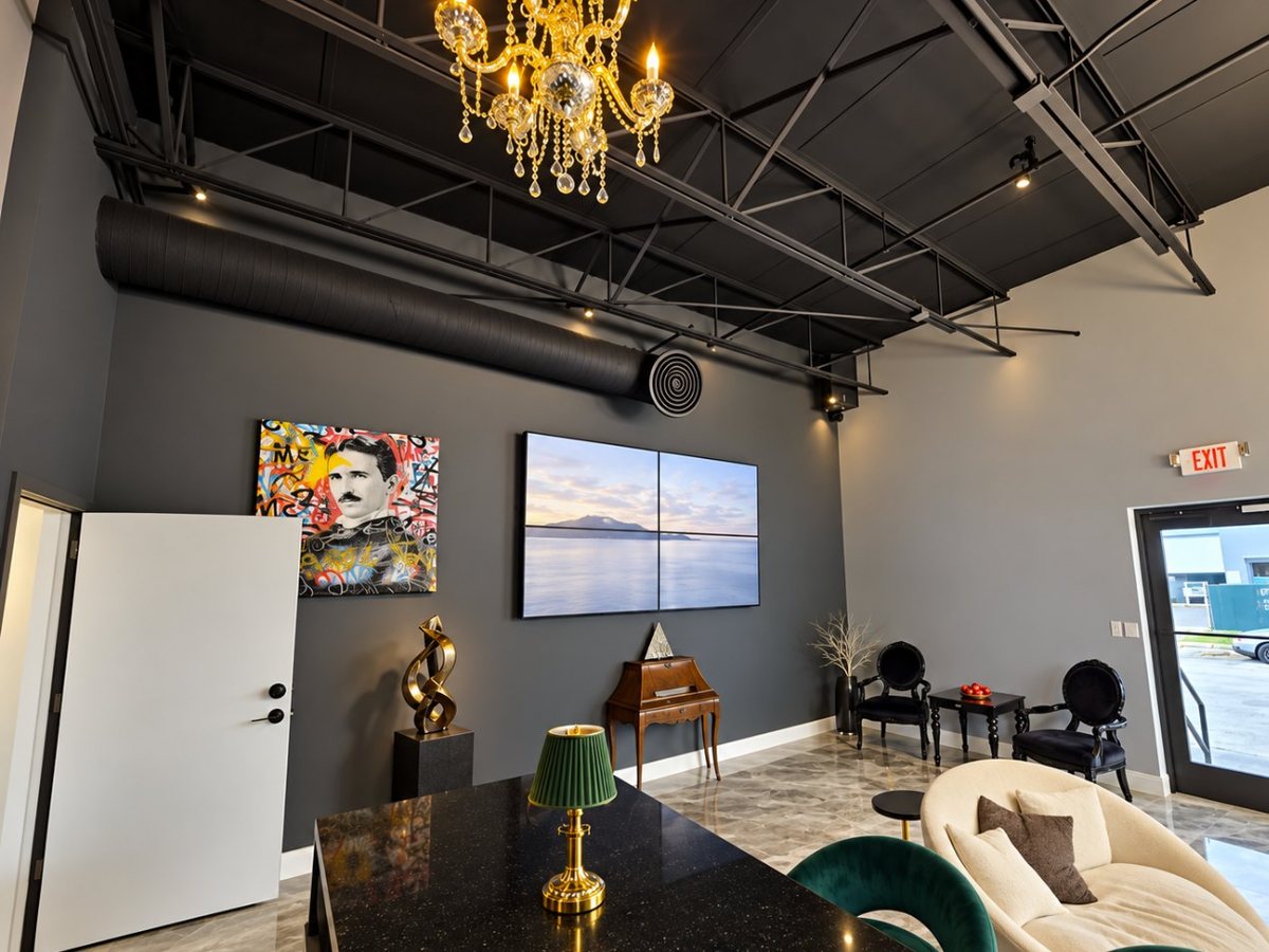 A reception lounge with a chandelier, a video wall, a cream sofa and black chairs
